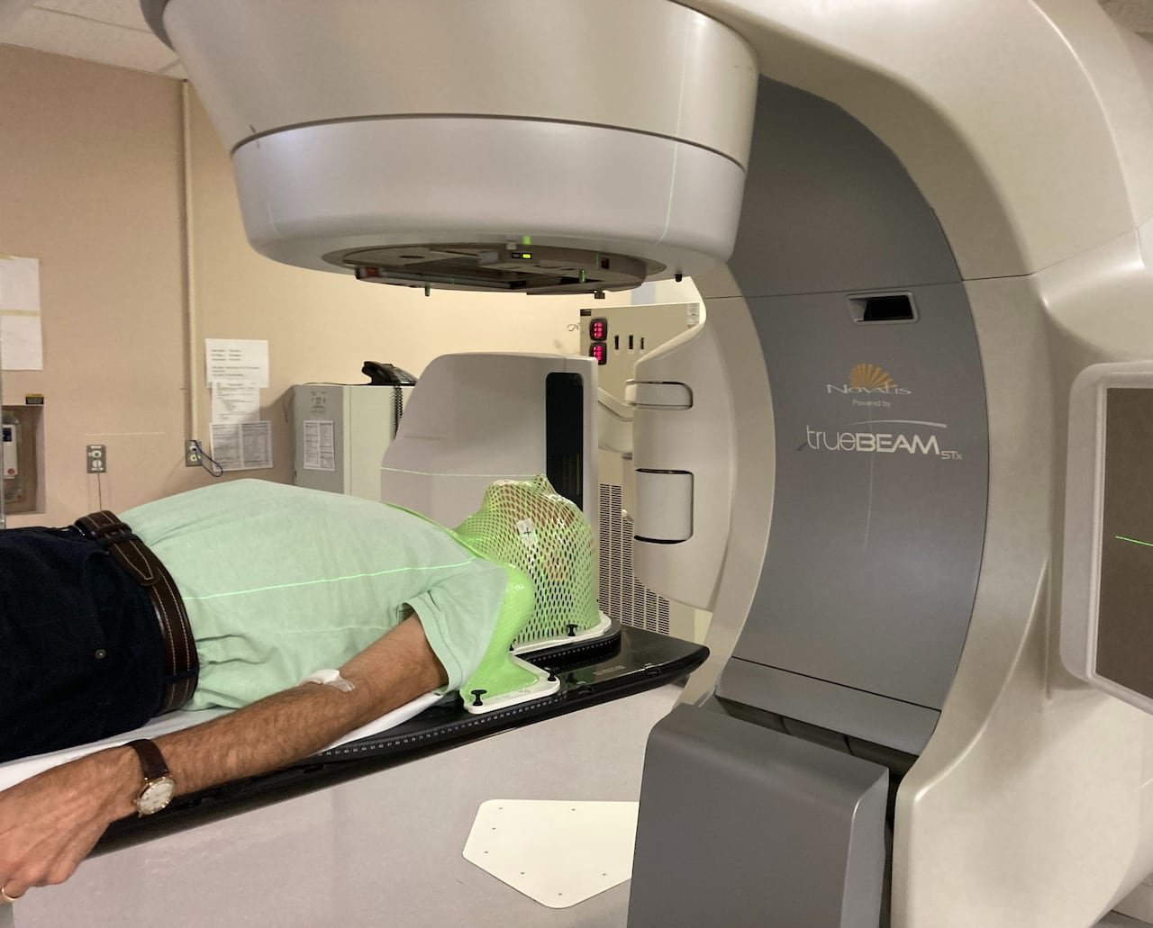 A man under a scanner, wearing a plastic targeting mask during his throat radiation treatment.